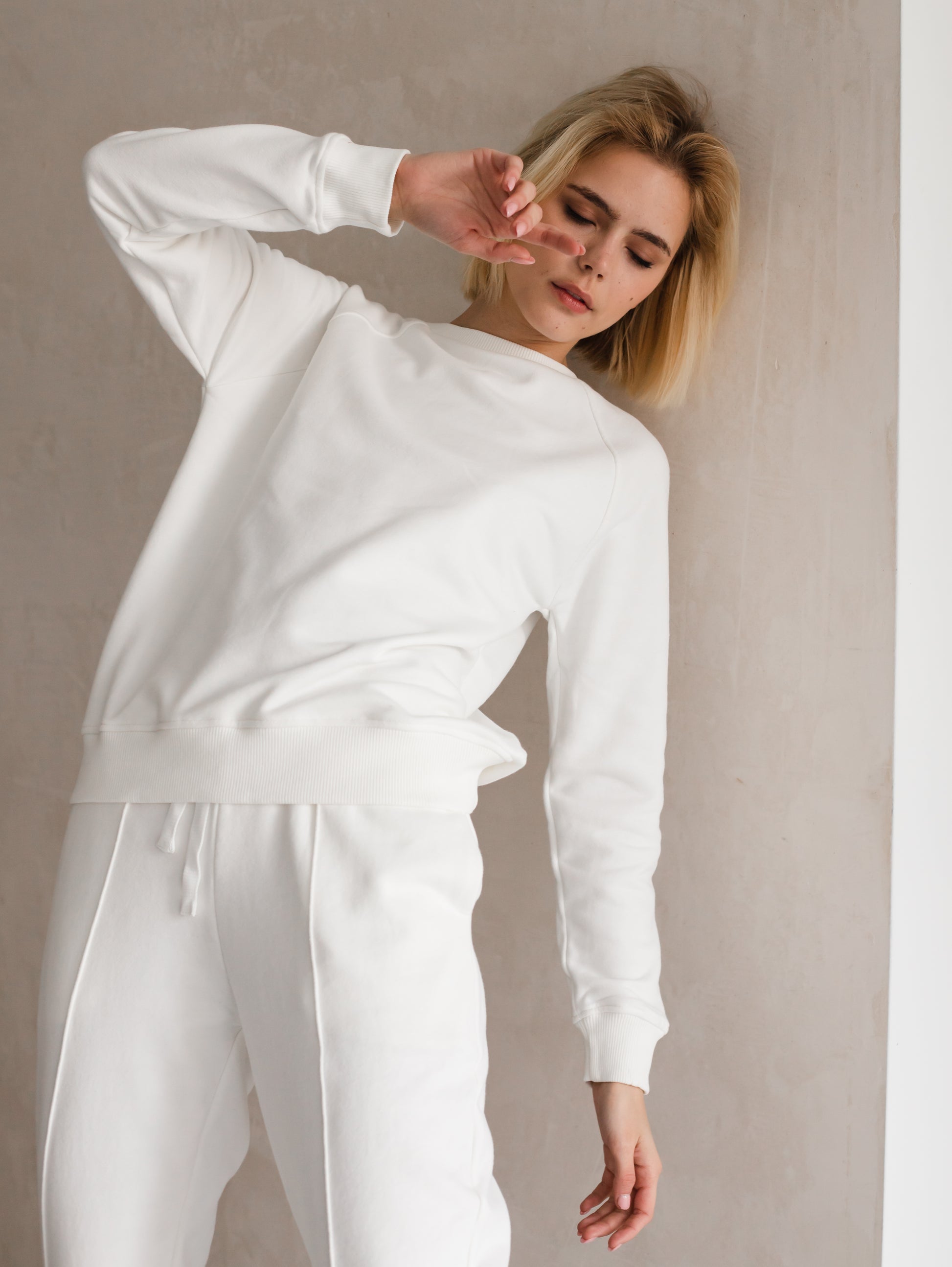 White joggers on model in front of a mirror – model wearing off-white joggers, back view reflected in a mirror, emphasizing the elegant and clean look of the fabric.